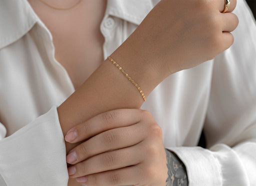Close-up of a person wearing a gold bracelet on a white shirt background