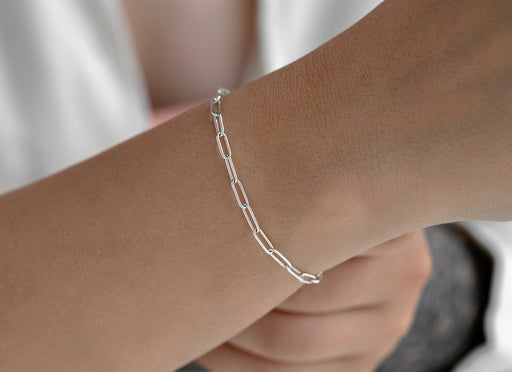 Silver chain bracelet on a wrist with a neutral background