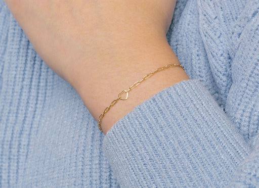 A gold heart-shaped wire charm connector worn as a bracelet on a person's wrist, with a sweater in the background.