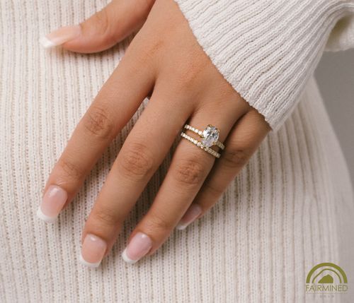 Hand model wearing Pear-Shaped Diamond Pavé Engagement Ring Semi-Mount in Fairmined Yellow Gold from RIVA Precision with matching wedding band