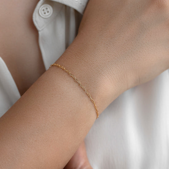 Gold paper-clip bracelet on a wrist with a white shirt background