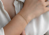 Gold paper-clip bracelet on a wrist with a white shirt background