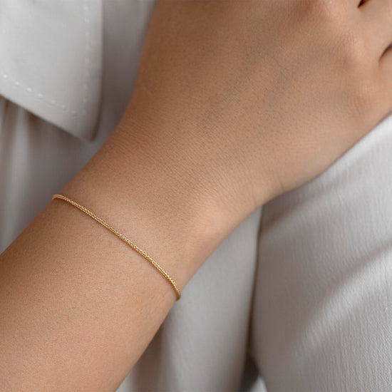 Gold bracelet on a person's wrist with a white shirt background