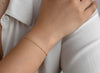 Gold bracelet on a person's wrist with a white shirt background