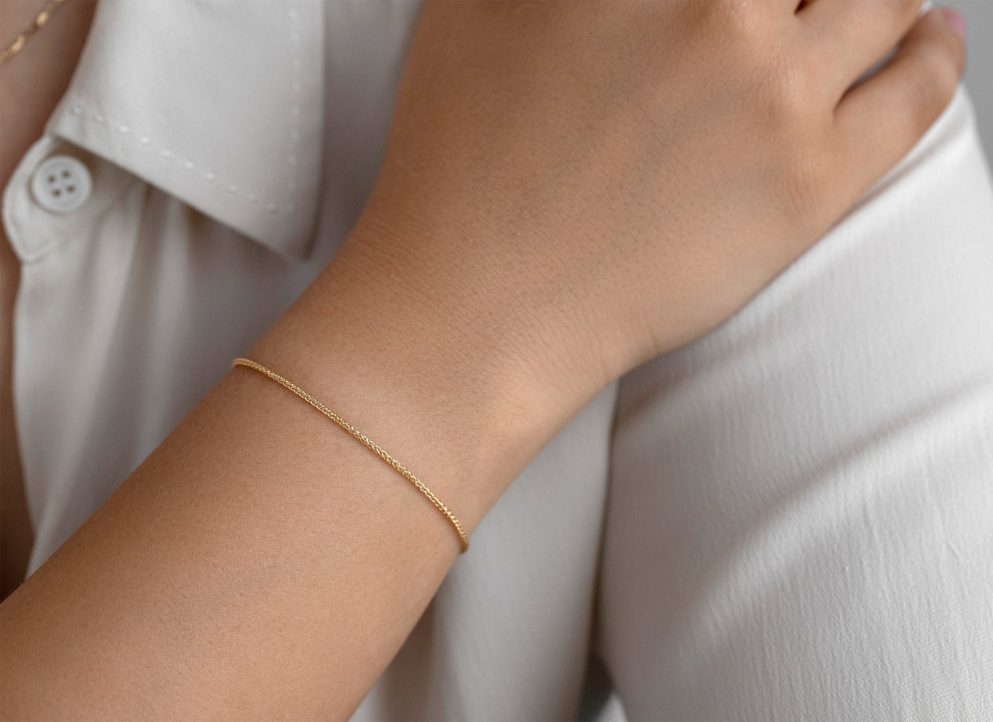 Gold bracelet on a person's wrist with a white shirt background