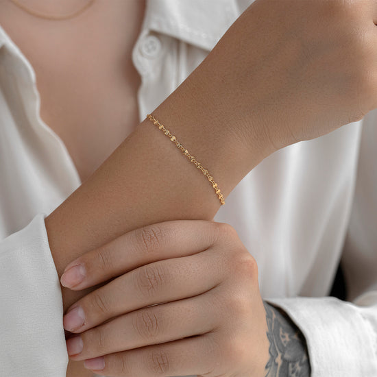 Close-up of a person wearing a gold bracelet on a white shirt background