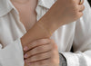 Close-up of a person wearing a gold bracelet on a white shirt background