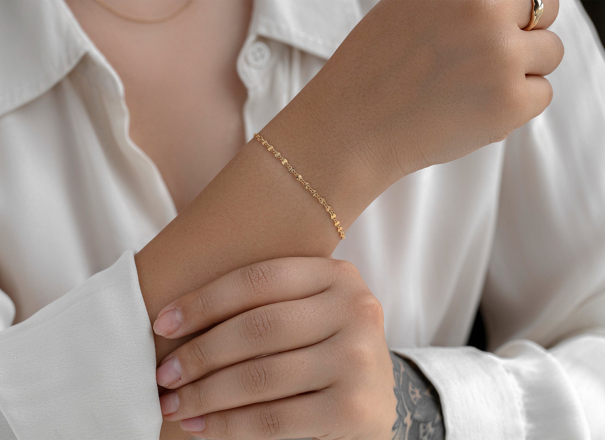 Close-up of a person wearing a gold bracelet on a white shirt background