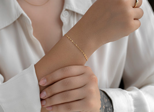 Close-up of a person wearing a gold bracelet on a white shirt background