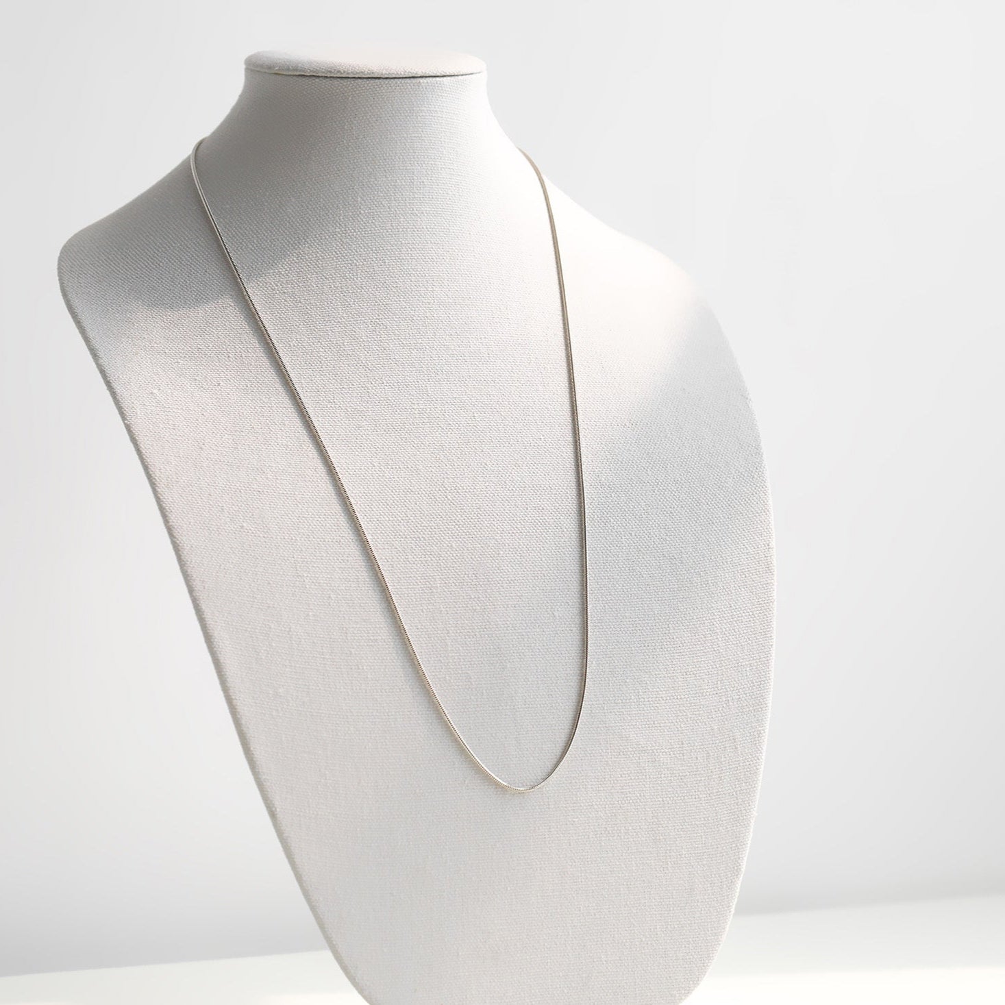 Silver necklace on a mannequin bust against a white background