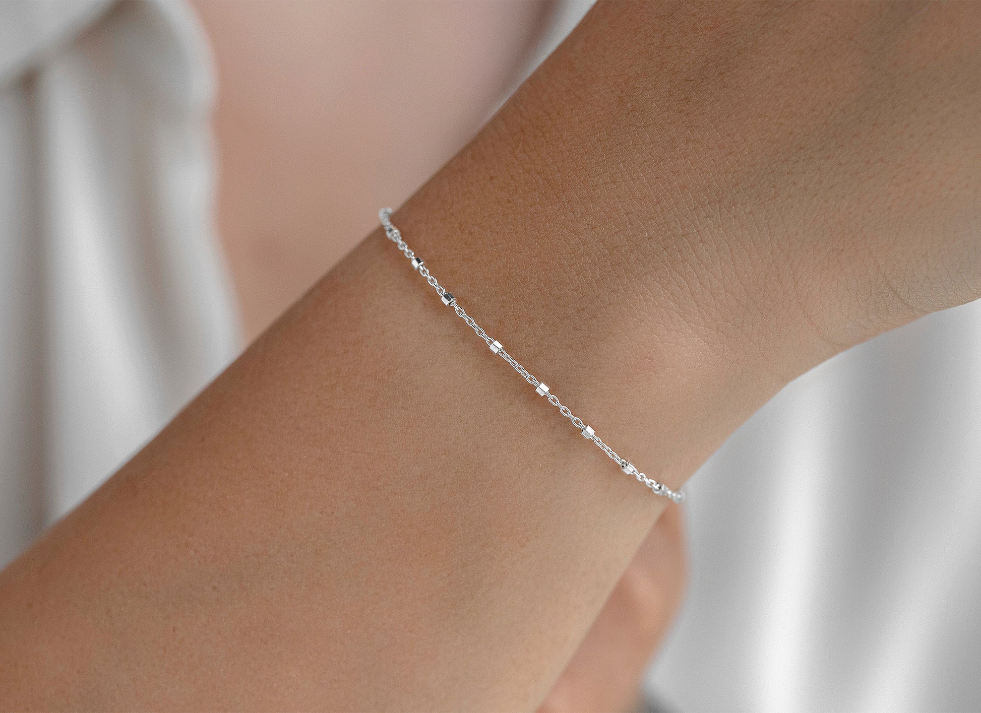 Silver cable satellite bracelet on a wrist with a neutral background