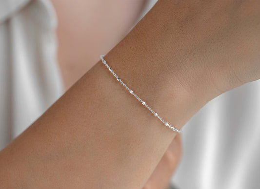 Silver cable satellite bracelet on a wrist with a neutral background