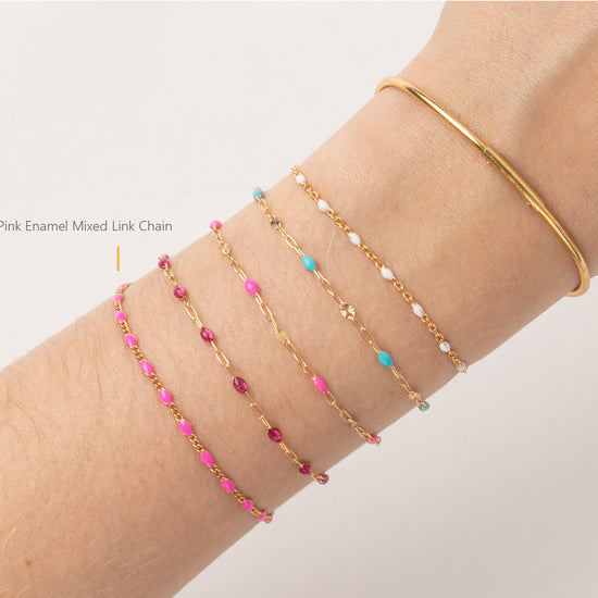 Gold bracelet with pink and blue beads on a wrist against a light gray background