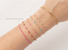 Gold bracelet with pink and blue beads on a wrist against a light gray background
