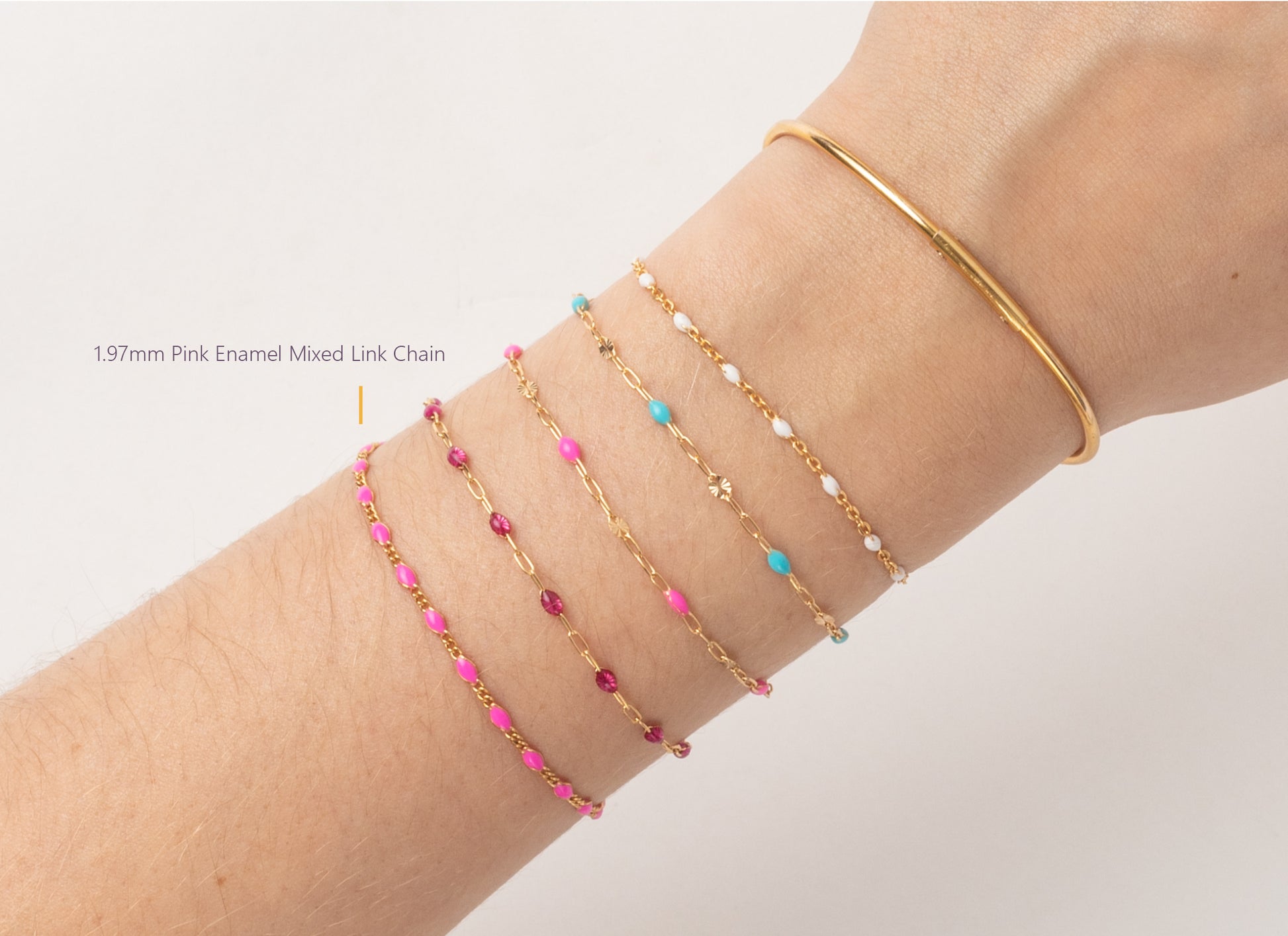 Gold bracelet with pink and blue beads on a wrist against a light gray background