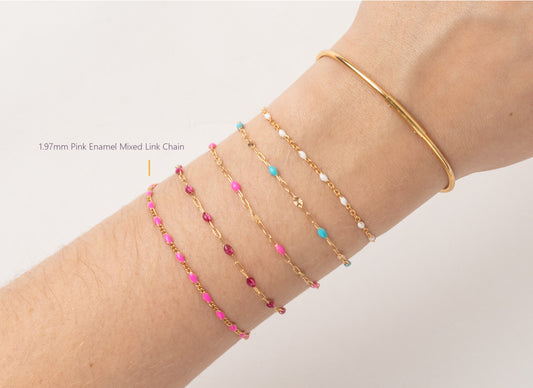 Gold bracelet with pink and blue beads on a wrist against a light gray background