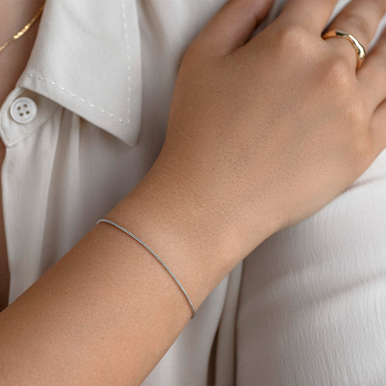 Close-up of a person wearing a gold ring and silver bracelet on a white shirt.