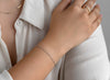 Close-up of a person wearing a gold ring and silver bracelet on a white shirt.