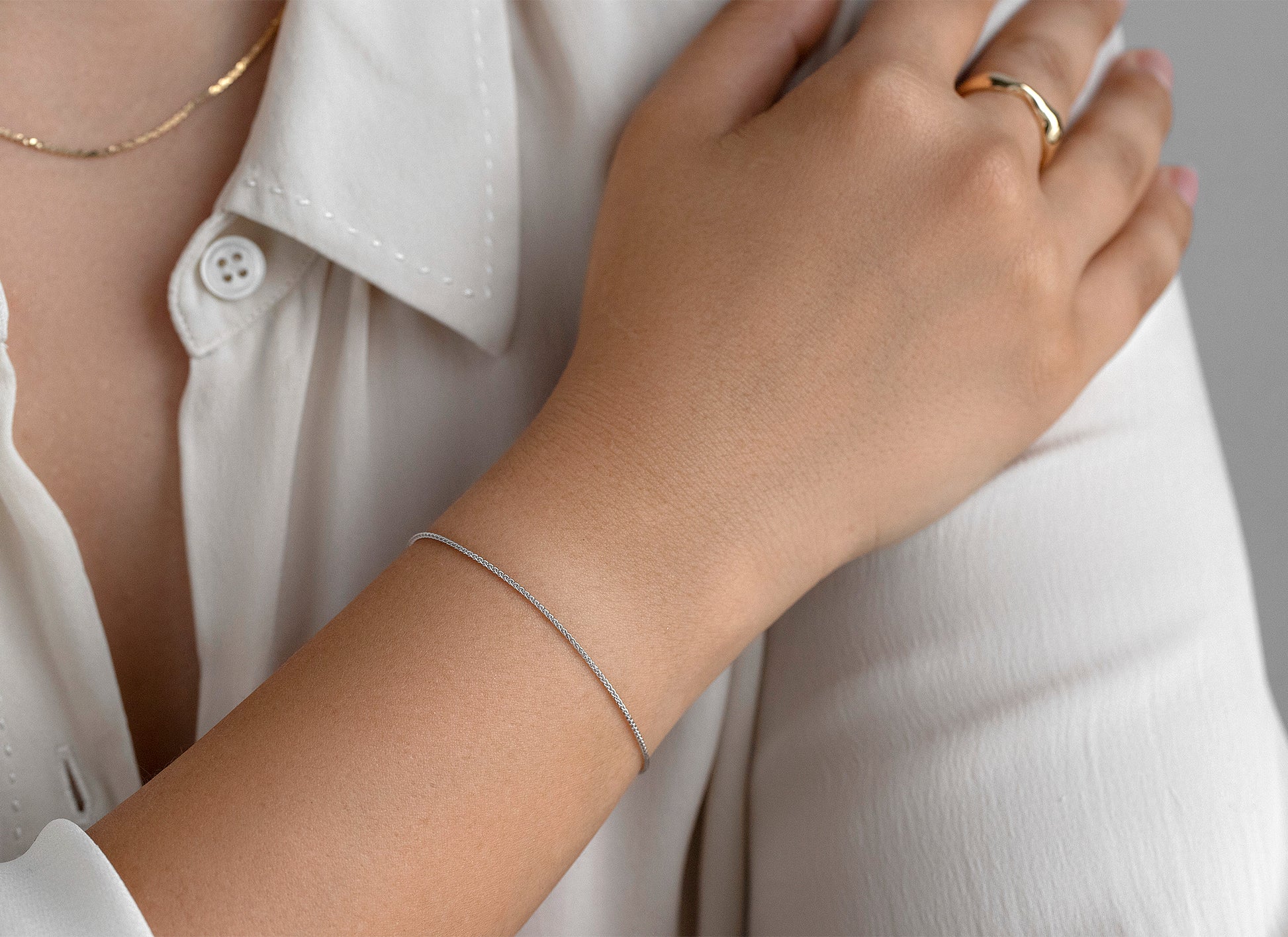 Close-up of a person wearing a gold ring and silver bracelet on a white shirt.