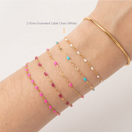 Gold bracelet with pink and blue beads on a wrist against a white background