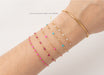 Gold bracelet with pink and blue beads on a wrist against a white background
