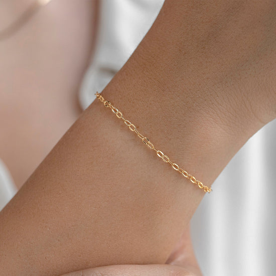 Gold bracelet on a person's wrist against a neutral background