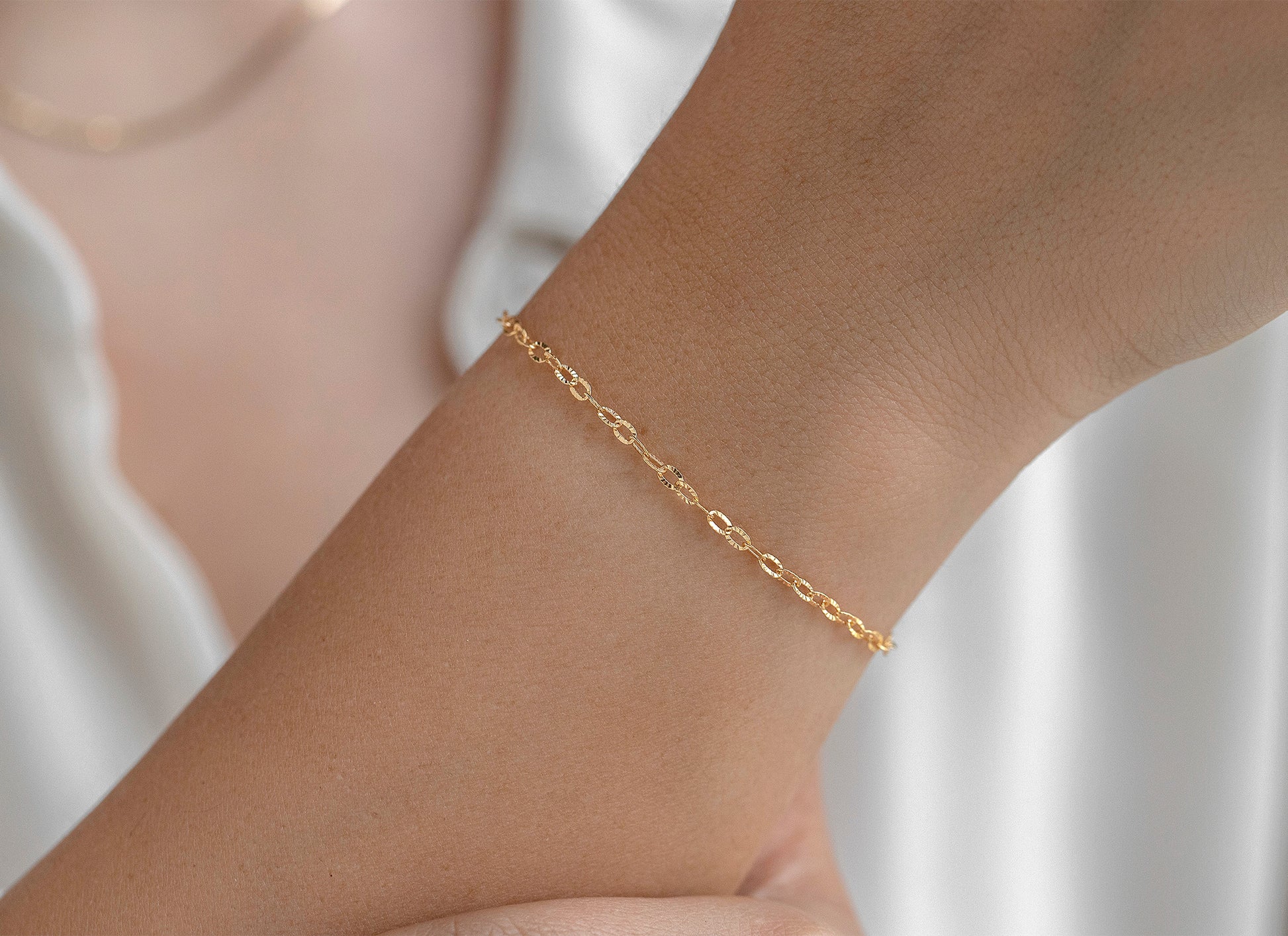 Gold bracelet on a person's wrist against a neutral background