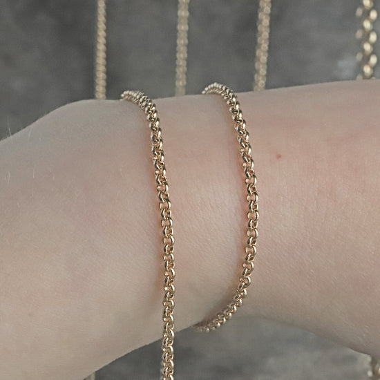 Gold fairmined rolo chain bracelet on a wrist with a blurred background
