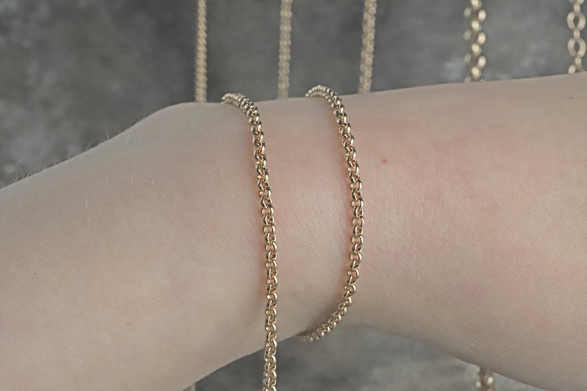 Gold fairmined rolo chain bracelet on a wrist with a blurred background