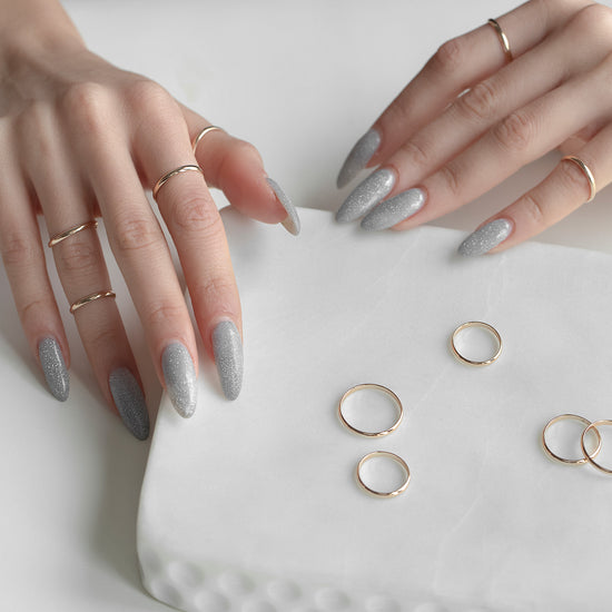Hands with gray nail polish holding a white cushion with gold rings on a light background