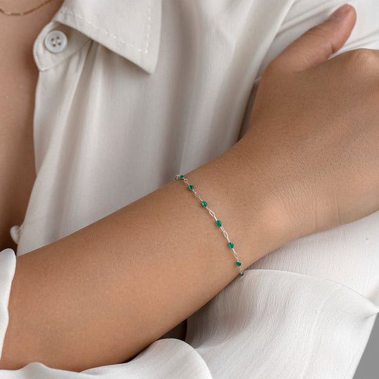 Person wearing a white shirt with a green enameled bracelet on a neutral background