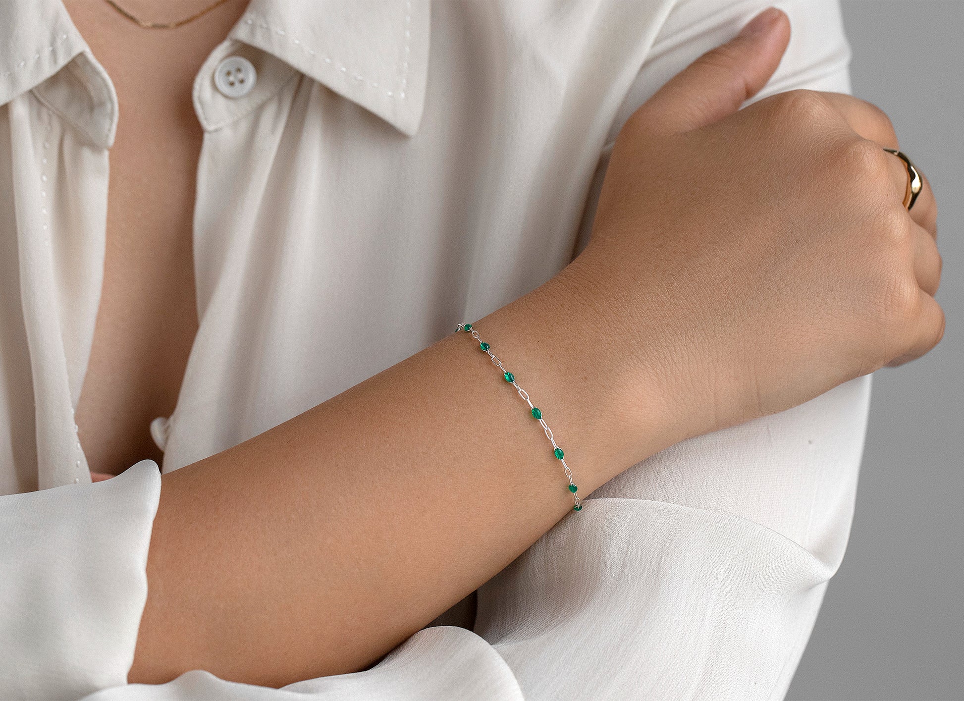Person wearing a white shirt with a green enameled bracelet on a neutral background