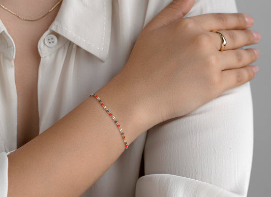 Hand wearing a bracelet and ring on a neutral background