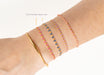 Close-up of a wrist wearing a gold bracelet and colorful beaded bracelets on a white background