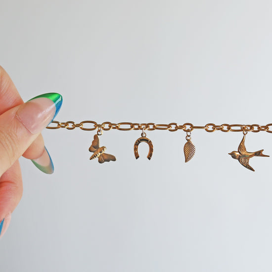 Gold bracelet with charms held by a hand against a light background