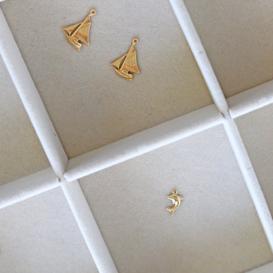 Gold sailboat-shaped earrings on a grid-patterned surface