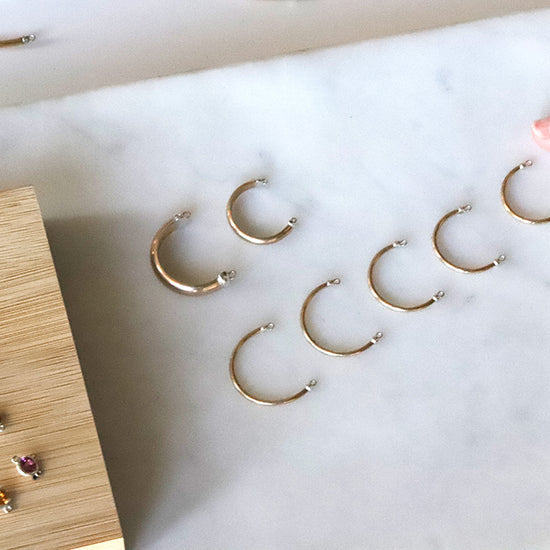 Gold permanent rings on a marble surface with a hand reaching towards them.