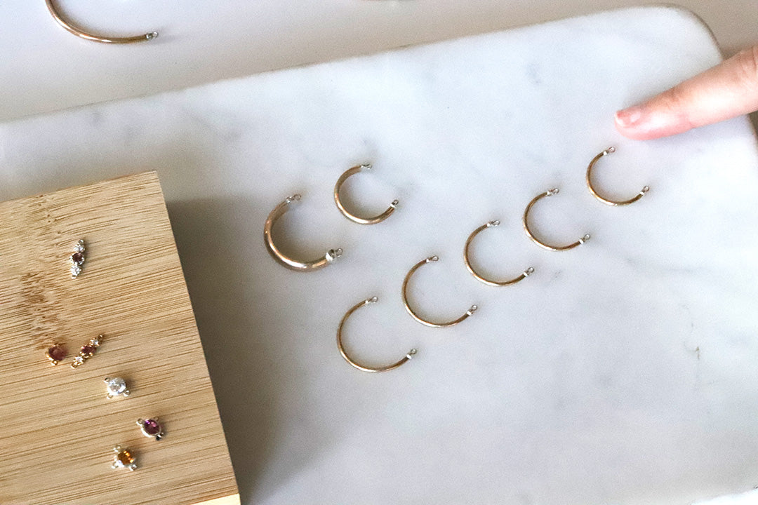 Gold permanent rings on a marble surface with a hand reaching towards them.