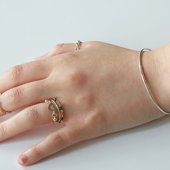 Hand wearing multiple rings and a bracelet on a light background