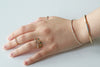 Hand wearing multiple rings and a bracelet on a light background