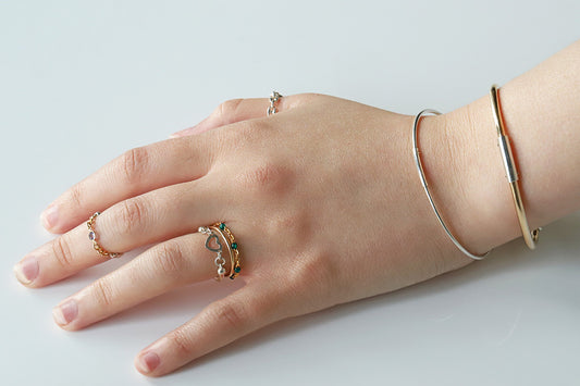 Hand wearing multiple rings and a bracelet on a light background