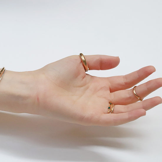 Hand wearing gold rings and a bracelet on a light background