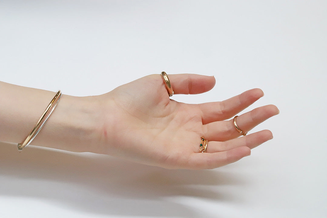 Hand wearing gold rings and a bracelet on a light background