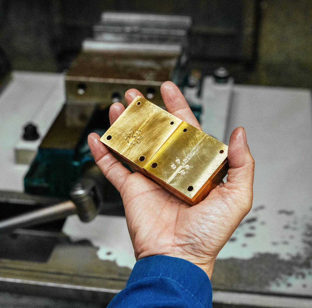Hand holding a gold metal block with a workshop in the background