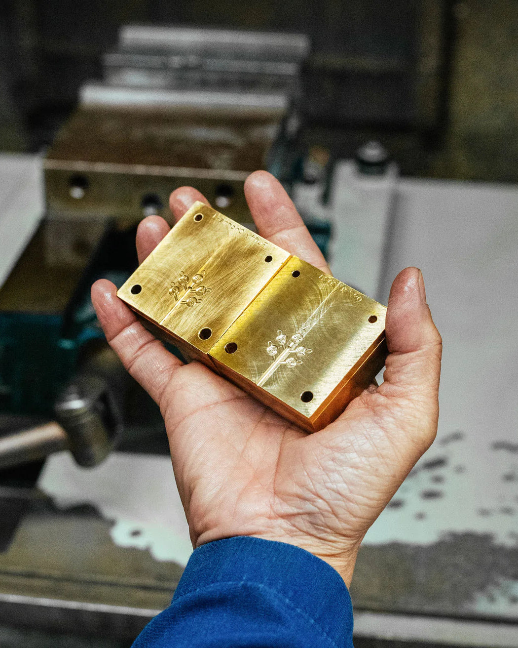 Hand holding a gold metal block with a workshop in the background
