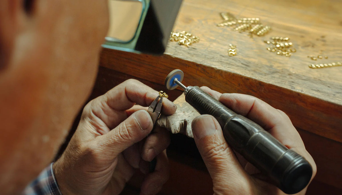 Person using a small tool on a piece of jewelry with a wooden surface in the background