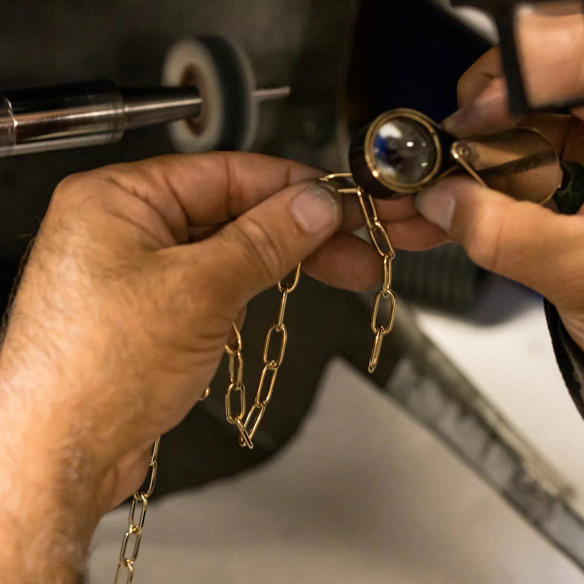 Person inspecting a gold chain with a magnifying glass in a workshop setting