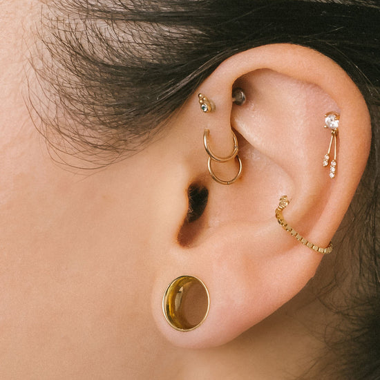 Close-up of an ear with multiple gold earrings on a neutral background