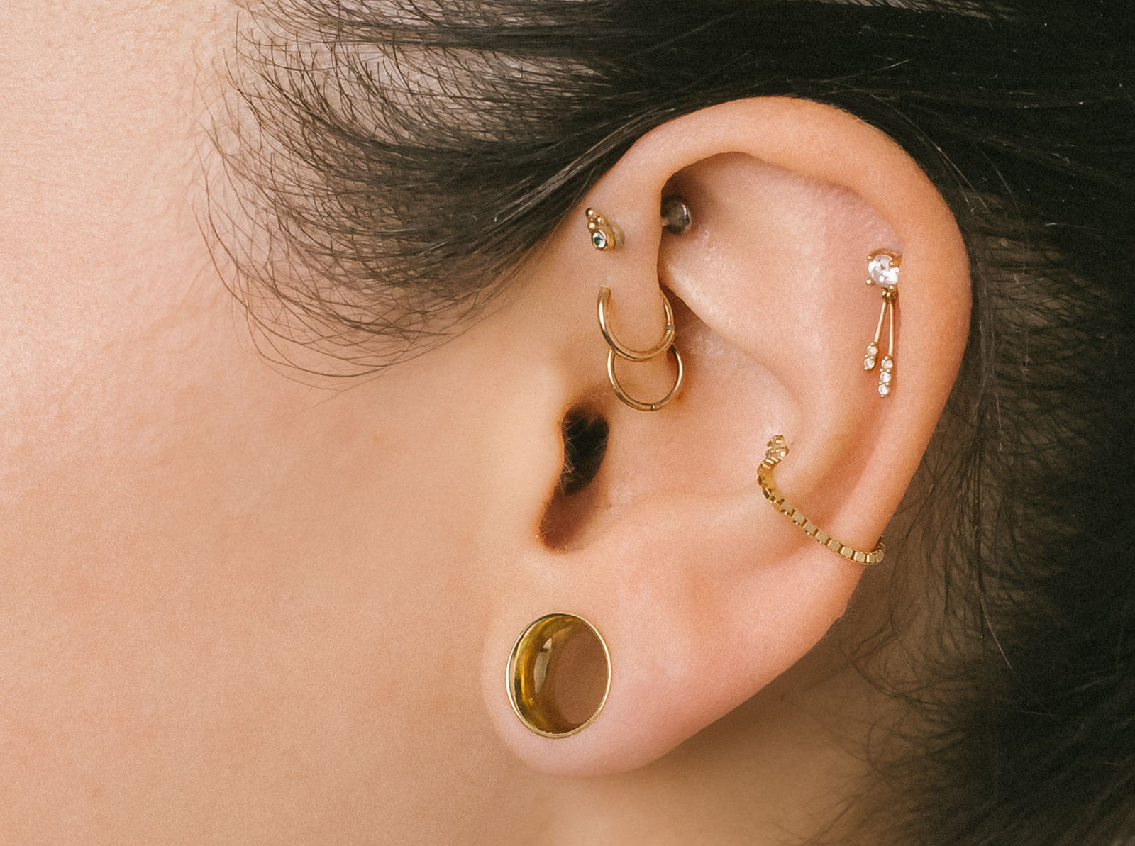 Close-up of an ear with multiple gold earrings on a neutral background