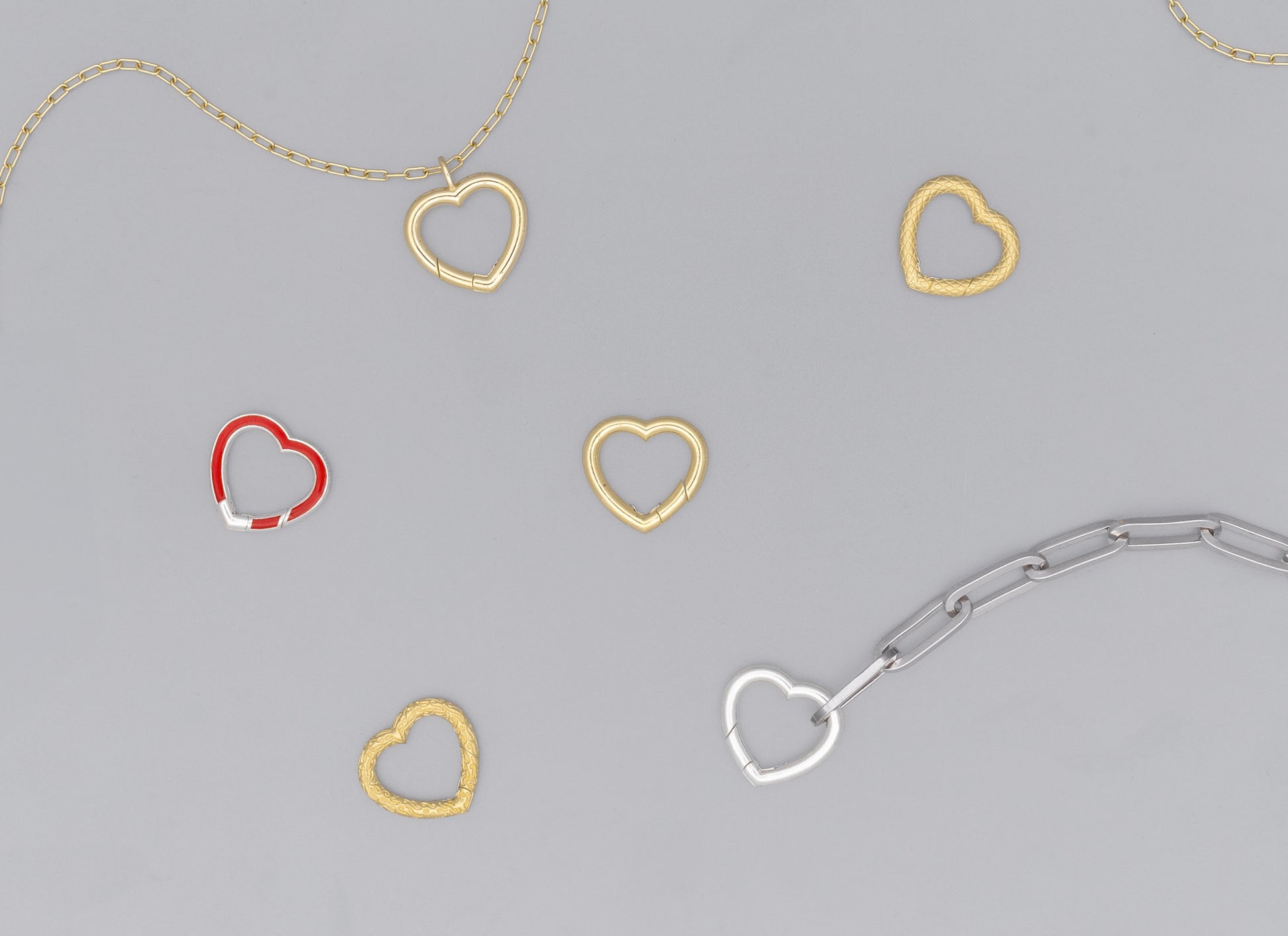 A series of heart-shaped invisible clasps in gold, silver, and red colors placed on a chain necklace.
